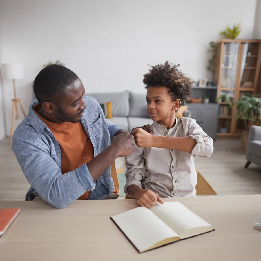 Male clinician sits at a table with child client, gives him a fist-bump