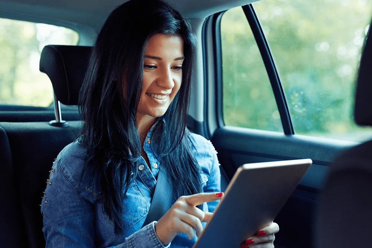 Smiling woman taps on tablet, sitting in a car
