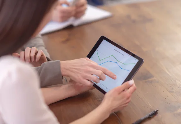 Two professionals sit at a desk reviewing data on a tablet